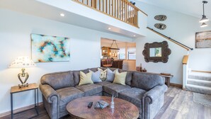A spacious living room with a sectional sofa, a coffee table, and a staircase leading to an upper level. - Riverwalk Retreat | Private Deck | Walk to Main St (Ouray)