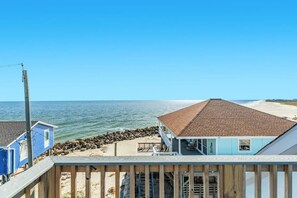 A beachfront property with a house featuring a tiled roof, a wooden deck, and a view of the ocean.