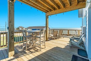 A wooden deck with outdoor furniture, including chairs and a table, overlooking a beach. - Beachpointe - Right by Beach, Sea For Miles! (Freeport)