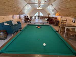A cozy room with a pool table, wooden furniture, and a large window.