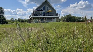 A two-story house with a balcony, surrounded by a grassy field.