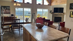 A spacious living area with a large wooden ceiling, a stone fireplace, and a dining area with a marble island.