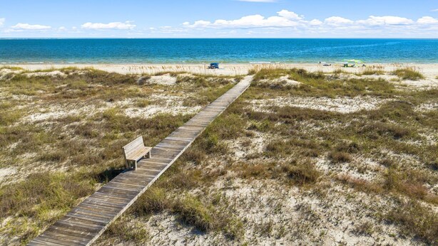 Une promenade en bois qui mène à une plage, avec un banc et une vue dégagée sur l’océan.