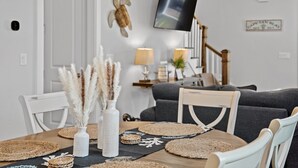 Un coin repas avec une table ronde, des chaises blanches et des sets de table en fibres tressées.