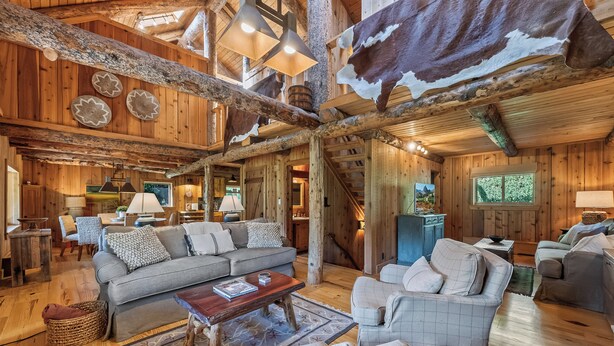 A rustic cabin interior with wooden walls, a fireplace, and a cozy seating area with sofas and a coffee table. - Solitude in Sundance - Hot Tub, 4 Bed 4 Bath, Secluded, Views, Quiet, Forested (Sundance)