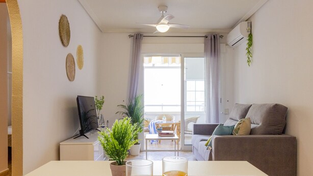 Un salon avec un canapé, un téléviseur, une table basse et une table à manger sur laquelle sont posés deux verres de jus d’orange.