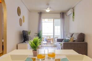 Ein Wohnzimmer mit einer Couch, einem Fernseher, einem Couchtisch und einem Esstisch mit zwei Gläsern Orangensaft.