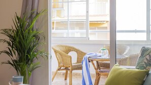 Une pièce dotée d’une grande fenêtre, de meubles en osier, d’une plante en pot et d’une table sur laquelle se trouvent une serviette et des bouteilles.