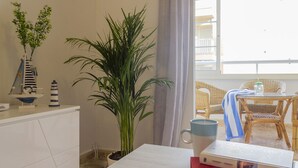 Une pièce avec un bureau blanc, une plante en pot, une maquette de petit voilier et une chaise en osier.