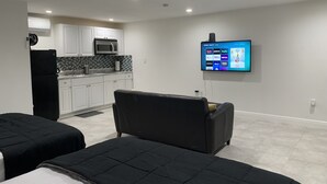 A modern hotel room with a kitchenette, a flat-screen TV mounted on the wall, and two black beds. - Beautiful Miami Pool Lake Studio (Cutler Bay)