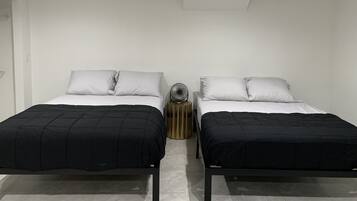 A room with two beds, each with a black and white bedspread, a small fan, and a nightstand with books.