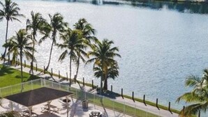 A swimming pool with lounge chairs and a view of a body of water and buildings in the background. - Beautiful Miami Pool Lake Studio (Cutler Bay)