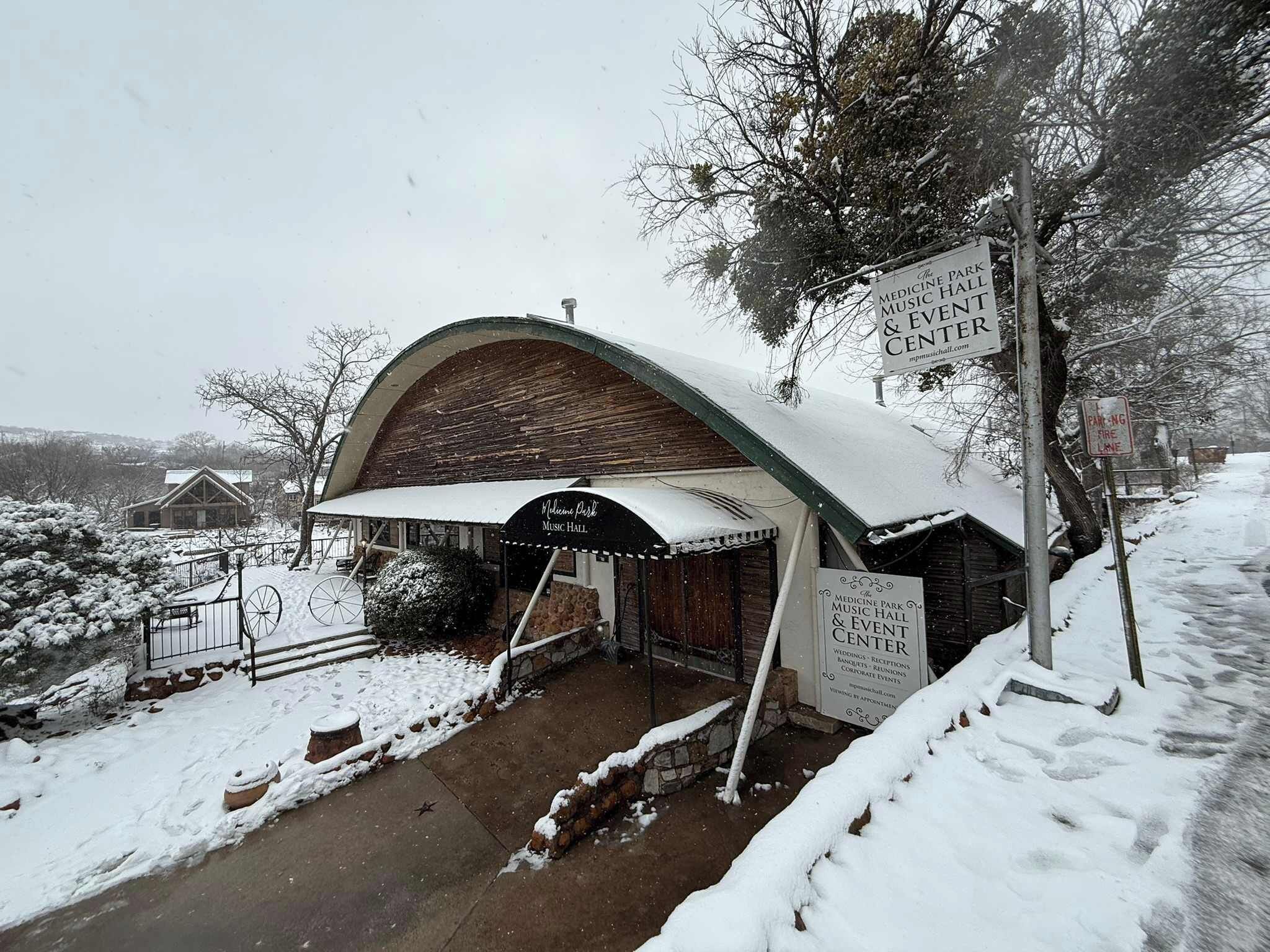 Un edificio cubierto de nieve con un cartel que anuncia el Medicine Park Music Hall & Event Center, indicando que alberga bodas, recepciones, banquetes y eventos corporativos.