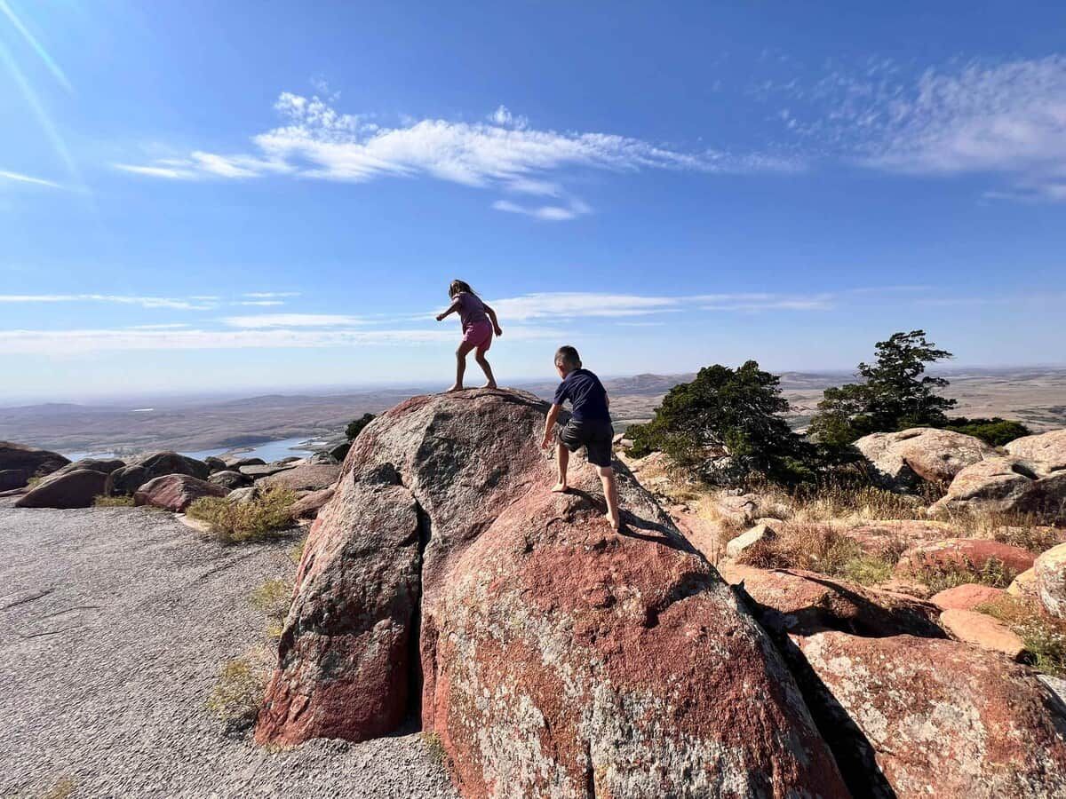 Two people standing on a large rock with a view of a landscape in the background.