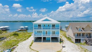 A two-story beachfront house with a balcony, a dock, and a beach view.