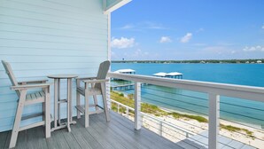A wooden deck with two chairs and a small table, overlooking a clear blue sea and a distant shoreline. - Luxury Lagoon Front Retreat | Private Pool | Pier and Beach Access (Gulf Shores)