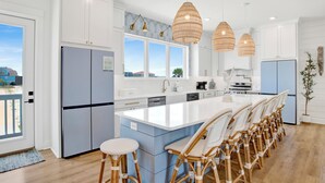 A modern kitchen with a large island, white cabinetry, and blue accents. - Luxury Lagoon Front Retreat | Private Pool | Pier and Beach Access (Gulf Shores)