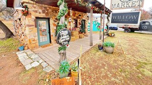 Edificio de piedra rústico con un porche de madera, adornado con follaje y decoraciones festivas. Un letrero anuncia limonada fresca, té helado y una compañía de bebidas.