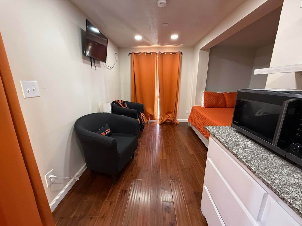 Een knus woongedeelte met een kitchenette, een flatscreen televisie aan de muur, een bank en een bed met oranje beddengoed.