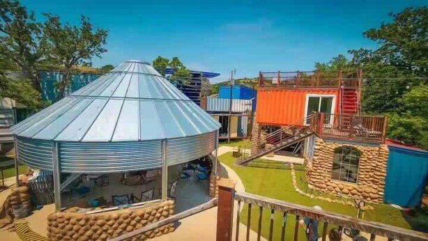Una estructura grande de varios niveles con techo cónico, rodeada de edificios y un área cercada con una piscina pequeña.
