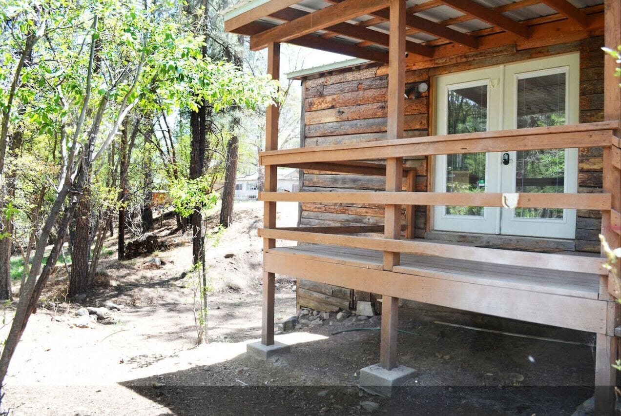 Una rustica baita di legno con veranda, circondata da alberi.
