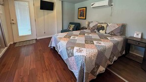 Une chambre avec un plancher en bois, un lit recouvert d’une courtepointe, une télévision et un climatiseur.