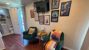 Un salon avec deux fauteuils verts, une petite table ronde et un téléviseur fixé au mur.