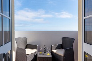 A balcony with two wicker chairs and a table, a bottle, and two glasses.