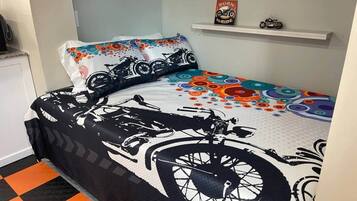 A bed with a black and white bicycle pattern, a colorful pillow, and a shelf with a motorcycle model.