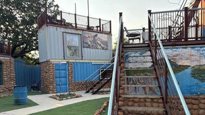 A building with a mural, a staircase, and a fenced area with outdoor seating.