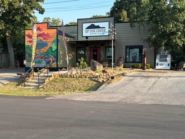A building with a sign reading 'UP THE CREEK SPIRITS' and a colorful mural on the left. - KB Book Fort Sill Tiny House, Slps 4 1BR/1BA. (Medicine Park)