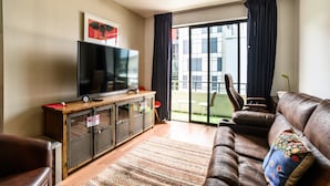 Ein Wohnzimmer mit Flachbildfernseher, Ledersofa und einer großen Schiebeglasdoor zum Außenbereich.