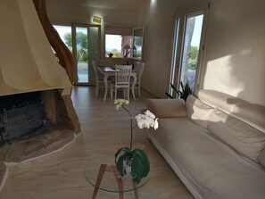 A modern living room with a beige sofa, a glass coffee table, and a dining area with white chairs. - Villa Giorgia – Sardinia, Orosei: An Entire House with Views of the Valley and the Sea (Orosei)