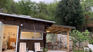 Een rustieke houten chalet met een overdekte veranda, buitenmeubels en een stenen muur op de achtergrond.