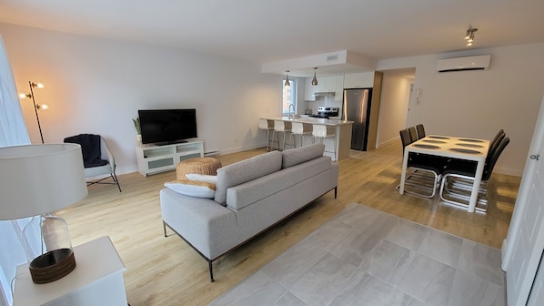 Una sala de estar moderna con un sofá gris, un televisor de pantalla plana y un comedor con mesa y sillas.