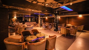 A dimly lit lounge area with wicker furniture and a bar in the background. - Maru Casa A City Center Hotel (Jaipur)