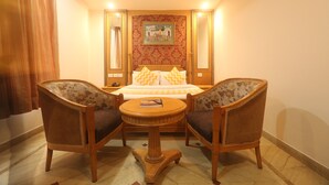 A hotel room with a bed, two armchairs, a small round table, and a painting on the wall. - Maru Casa A City Center Hotel (Jaipur)