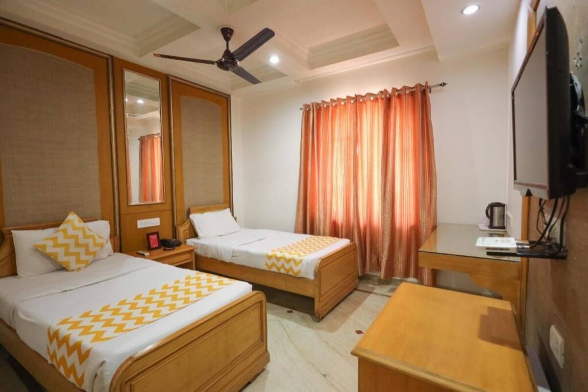 A hotel room with two beds, a desk, a television, and a ceiling fan.