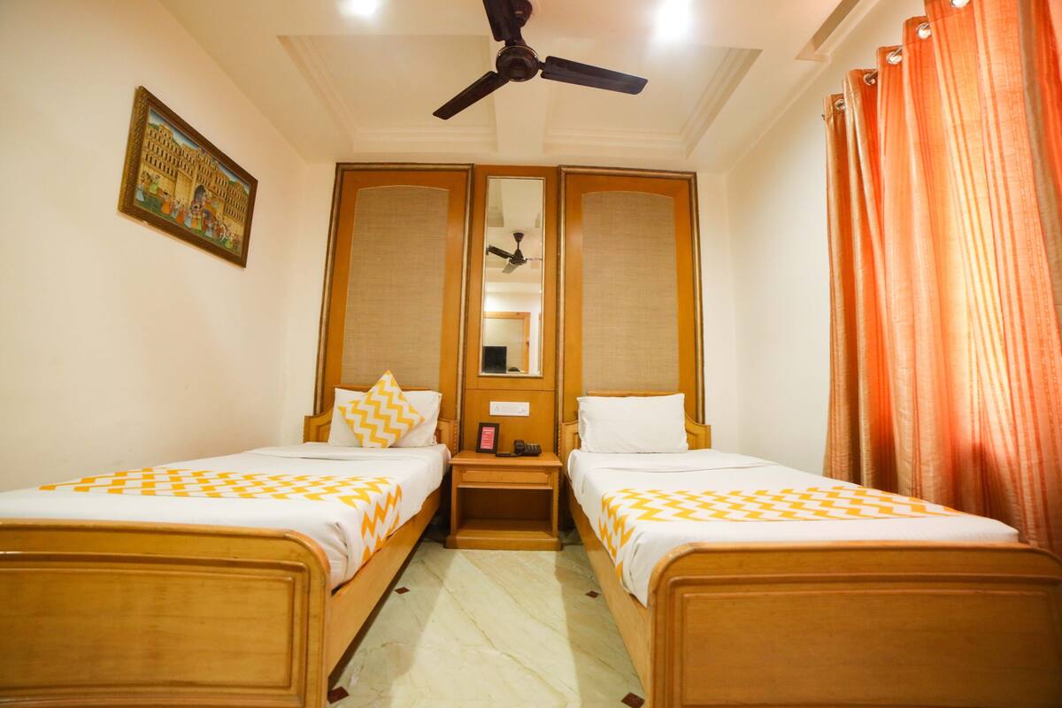 A hotel room with two wooden beds, a ceiling fan, a mirror, and a painting on the wall.