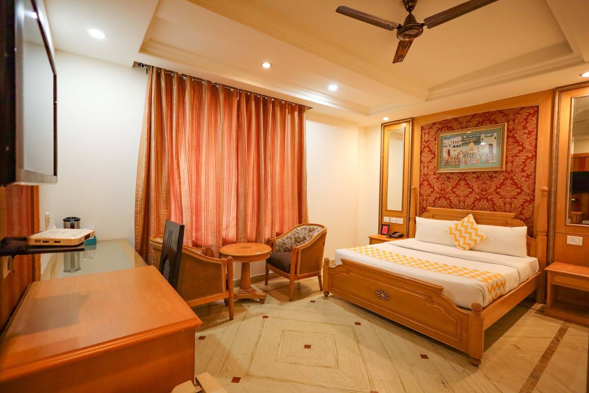 A hotel room with a bed, a desk, a chair, a small table, and a ceiling fan.