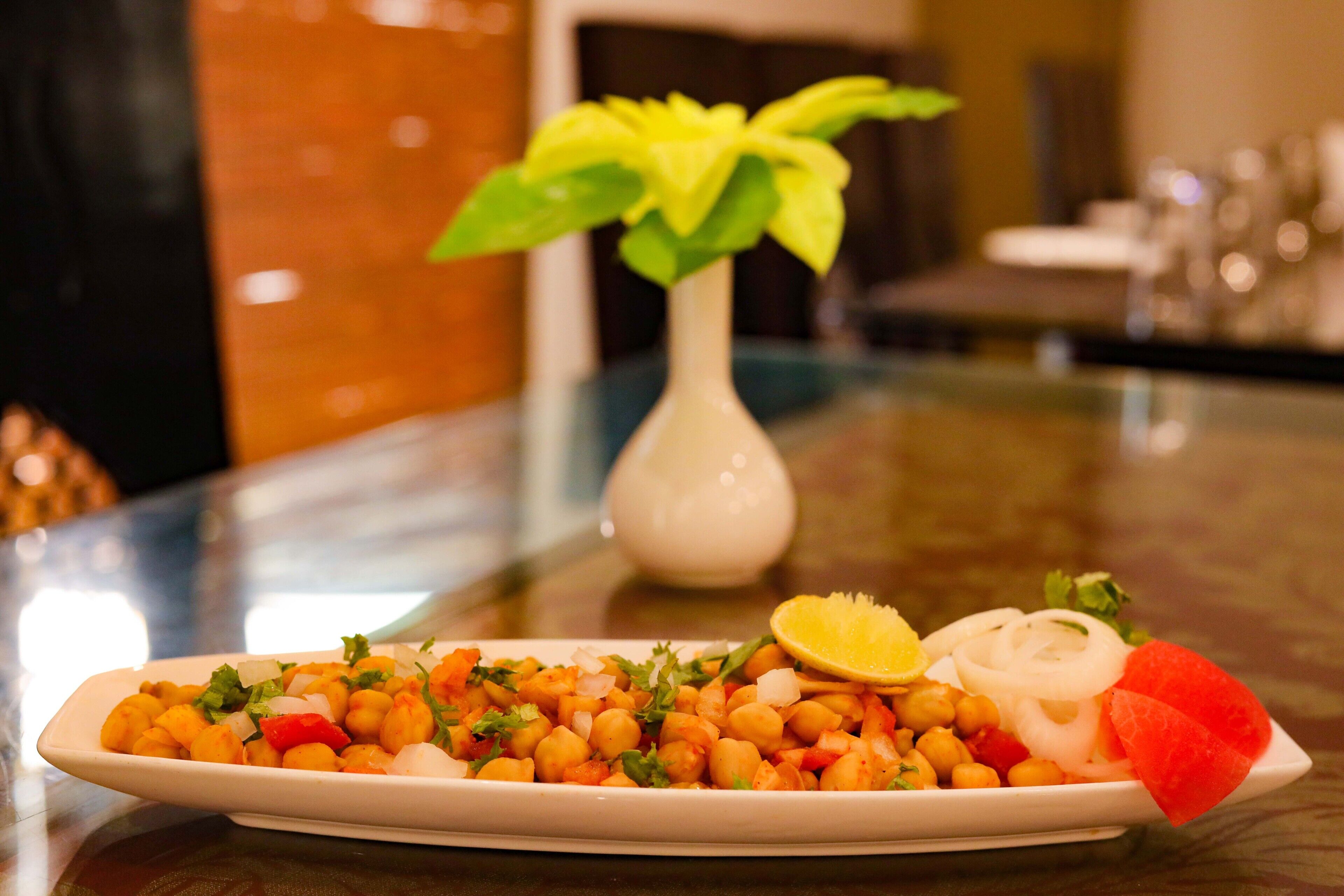 Une assiette de pois chiches accompagnée de légumes et d’un quartier de citron, posée sur une table.