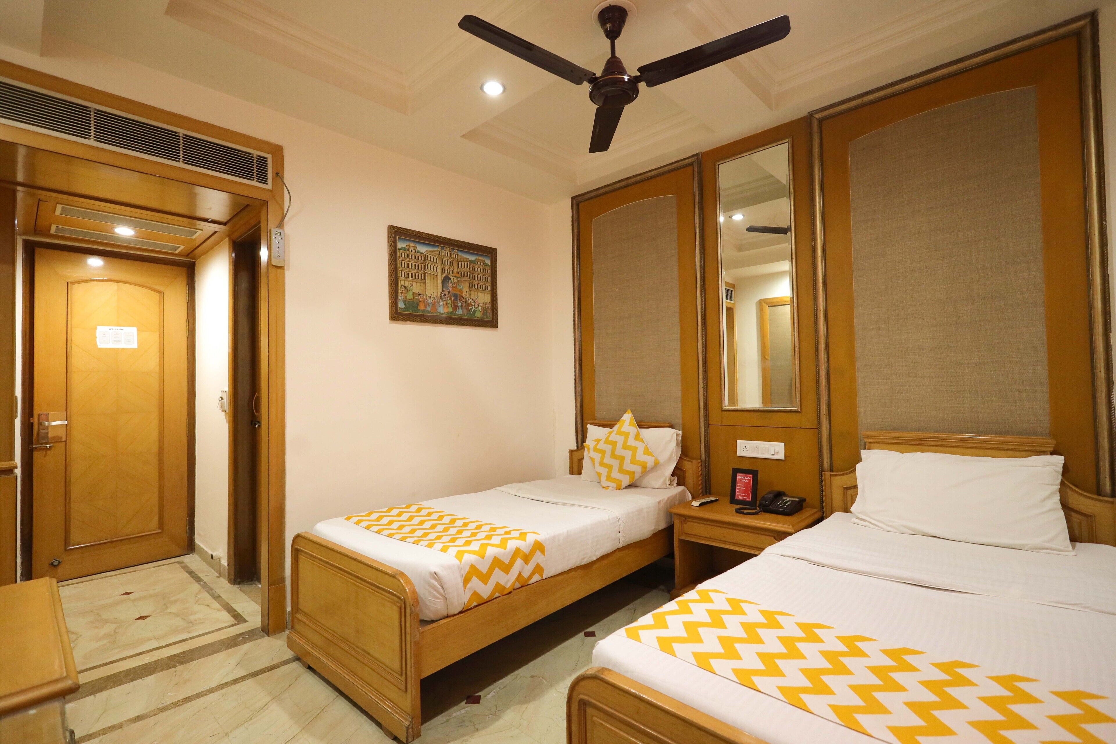 Habitación de hotel con dos camas individuales, un ventilador de techo, un cuadro en la pared y una puerta de madera.