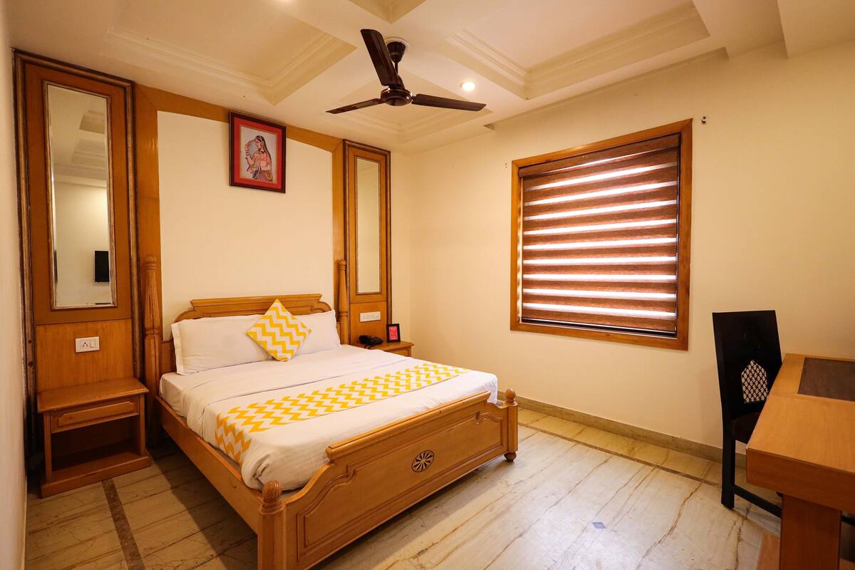 A bedroom with a wooden bed, a nightstand, a ceiling fan, a window with blinds, and a chair.