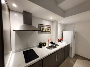 Una cocina moderna con estufa integrada, campana extractora de acero inoxidable, pileta con grifo rojo y refrigerador blanco.