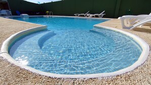Ein klarer Pool mit Kiesrand, umgeben von einer grünen Wand und weißen Liegestühlen.