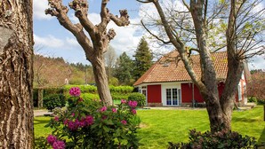 Ein rotes Haus mit Ziegeldach, umgeben von einem gepflegten Rasen und blühenden Büschen.