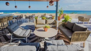 An outdoor seating area with wicker furniture, a round table, and potted plants. - 1BR Condo Best Location (Playa del Carmen)