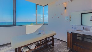A modern bathroom with a massage table, large windows with a view of the ocean, a vanity with a mirror, and a wall-mounted air conditioner. - 1BR Condo Best Location (Playa del Carmen)