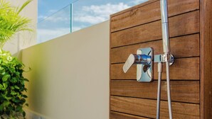 A wooden shower enclosure with a chrome showerhead and hose, adjacent to a glass wall and a wooden deck. - 1BR Condo Best Location (Playa del Carmen)