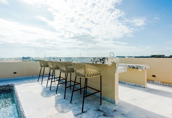 A rooftop terrace with a pool, three wicker bar stools, and a marble counter. - 1BR Condo Best Location (Playa del Carmen)